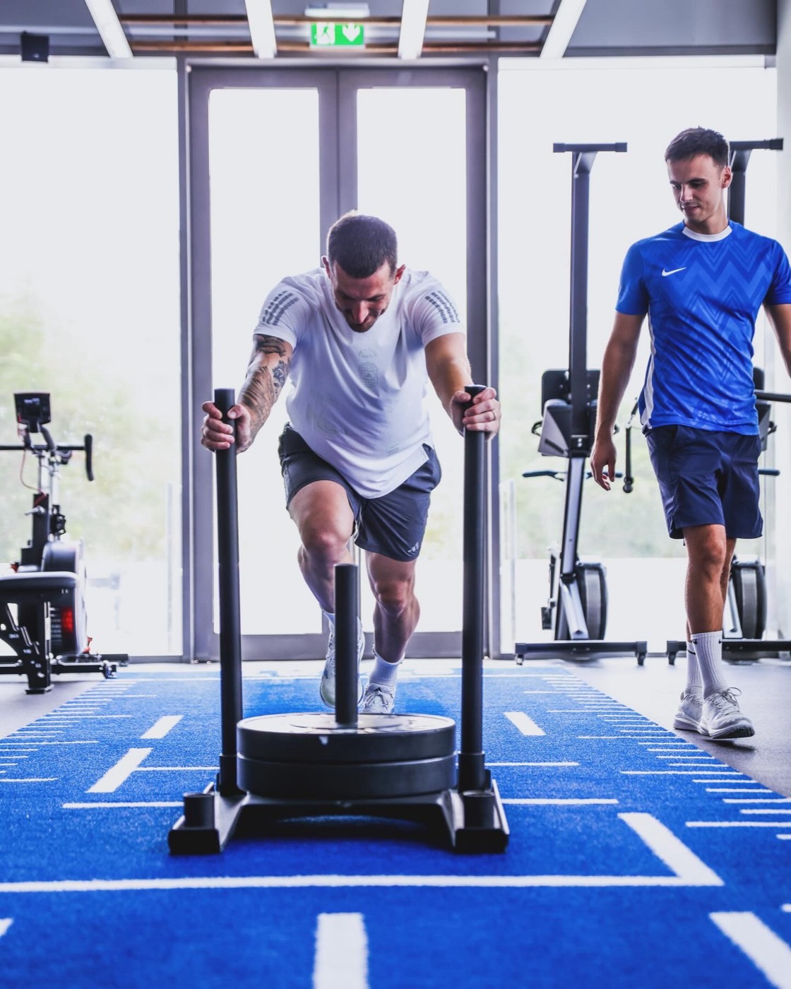 Athlet beim Sled Push auf blauem MYtrainingclub HYROX-Kunstrasen im Studio